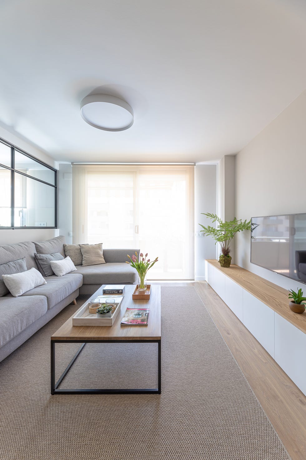 salón nórdico con sofá gris con chaise longue, mesa de madera y metal y muebles tv blanco con balda de madera