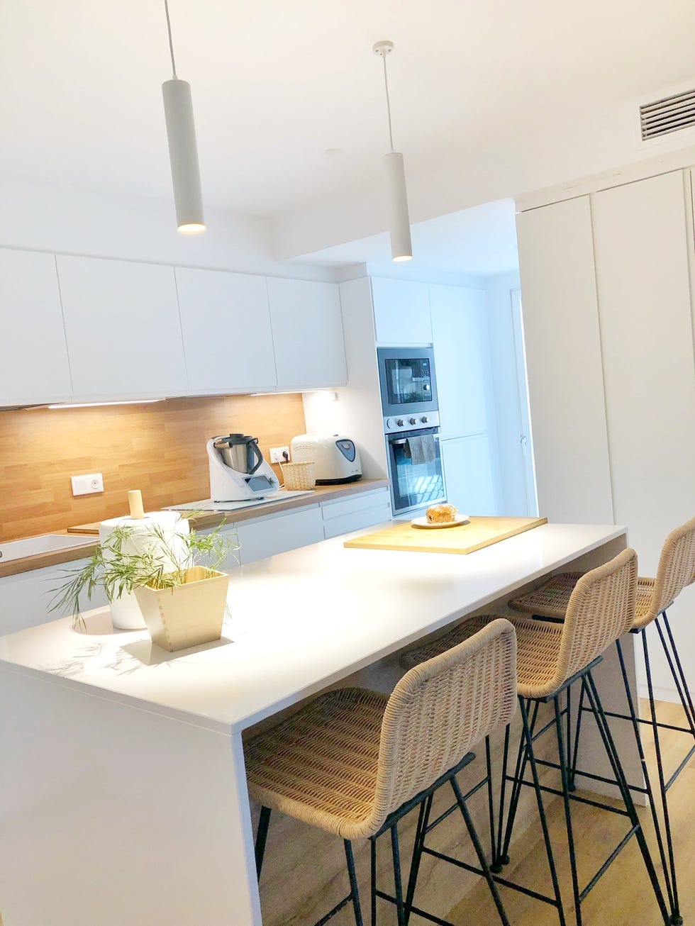 cocina blanca con isla central, taburetes de fibras y encimera y frente de madera