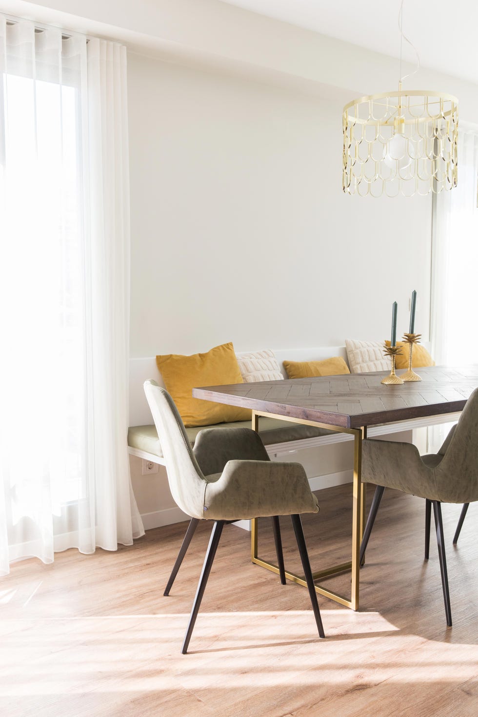 mesa de comedor de madera y latón, banco con cojines y sillas tapizadas en verde y lámparas suspendidas doradas