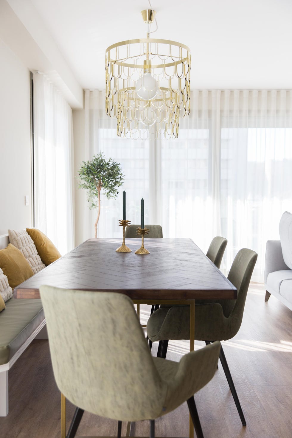 mesa de comedor de madera y latón, banco con cojines y sillas tapizadas en verde y lámparas suspendidas doradas