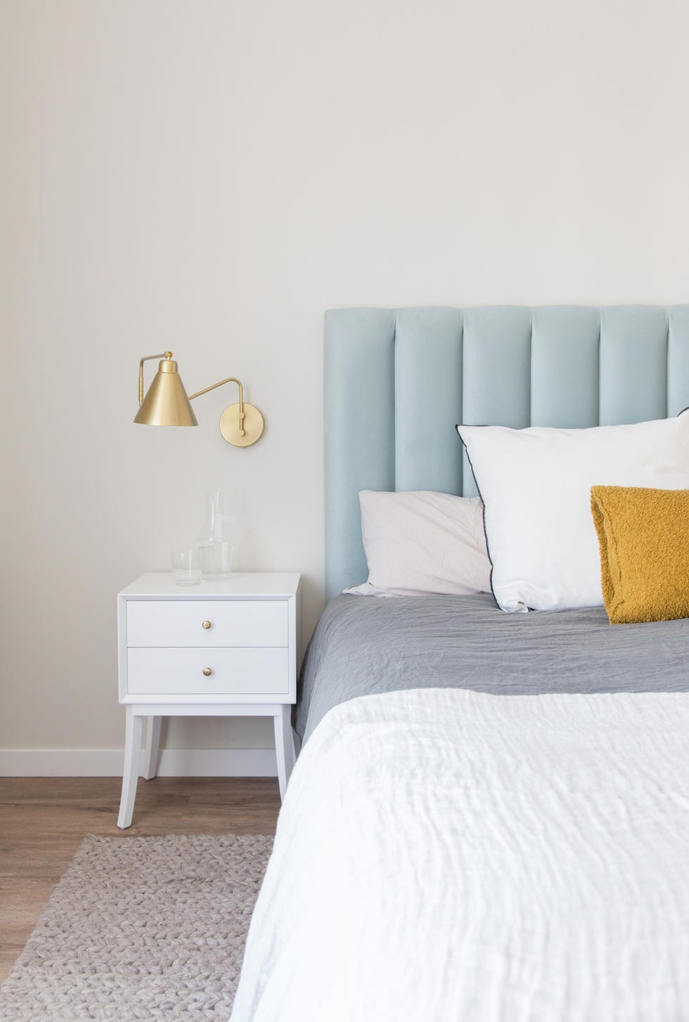 dormitorio con cabecero azul de terciopelo acolchado, mesita blanca y aplique dorado