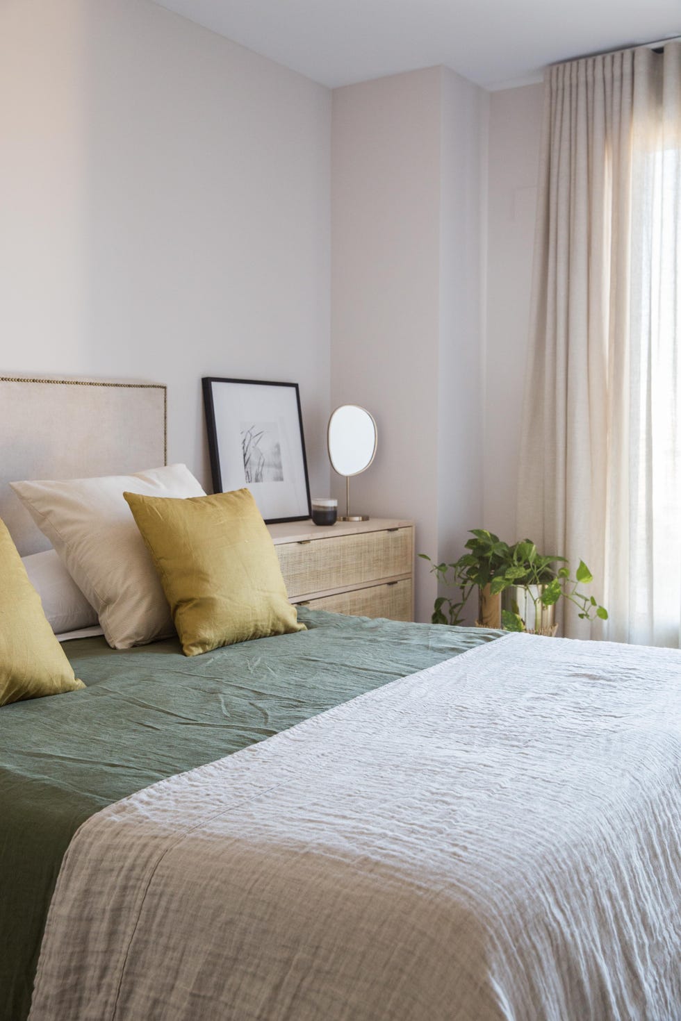 dormitorio con cabecero tapizado en lino, mesitas de madera y textiles verdes