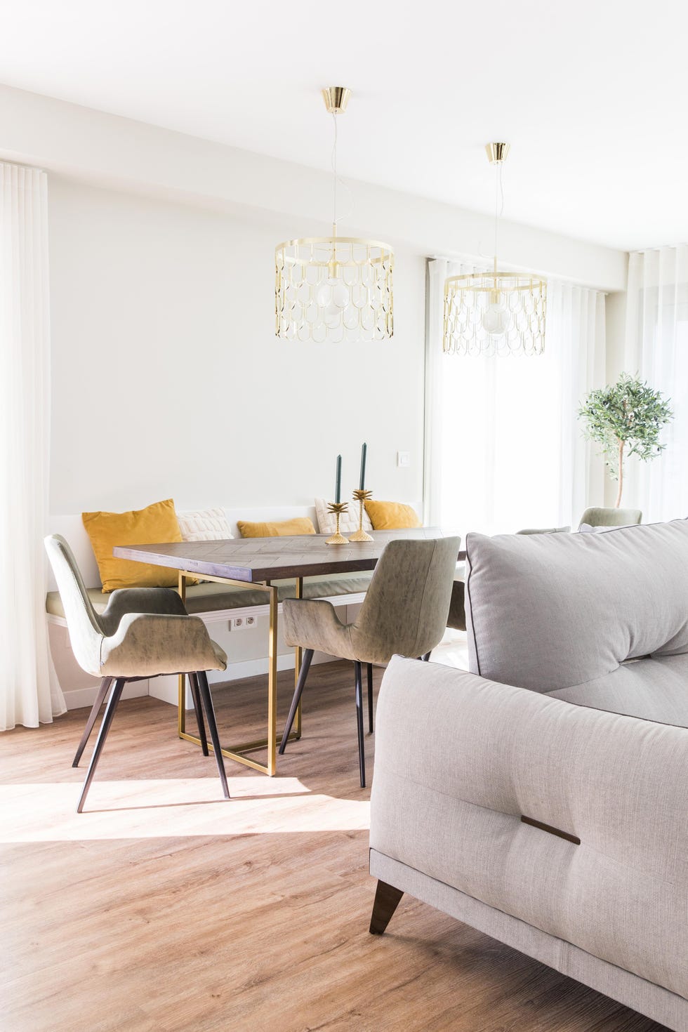 mesa de comedor de madera y latón, banco con cojines y sillas tapizadas en verde y lámparas suspendidas doradas
