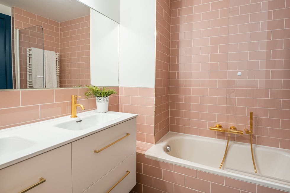 baño con bañera, azulejos tipo metro rosas y mueble blanco suspendido