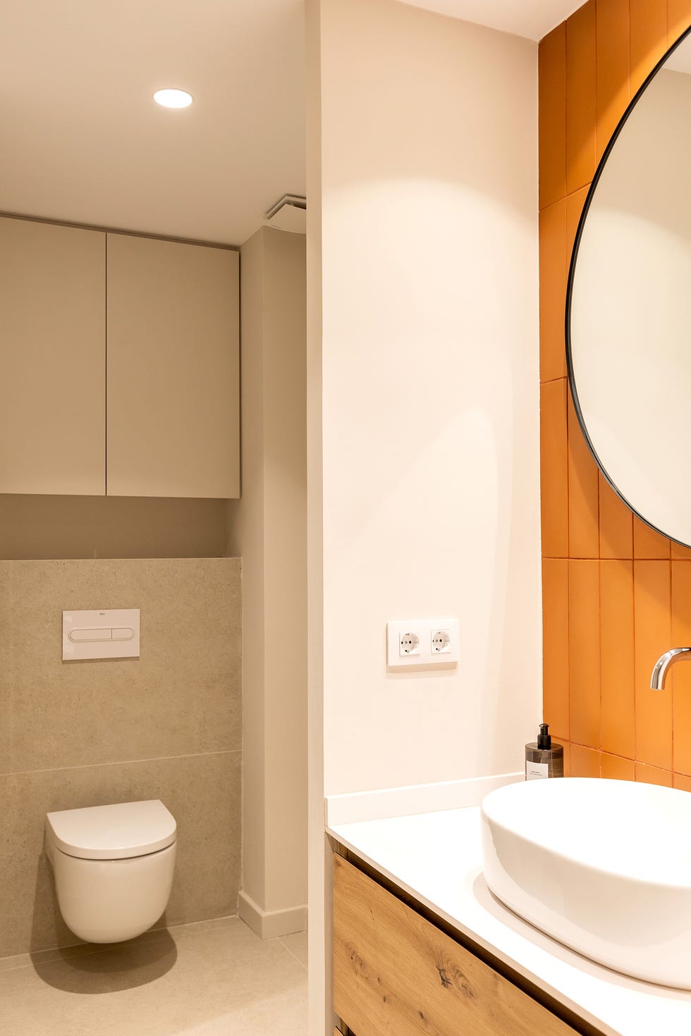 mueble de lavabo de madera con encimera blanca, lavamanos exento, espejo redondo y azulejos naranjas
