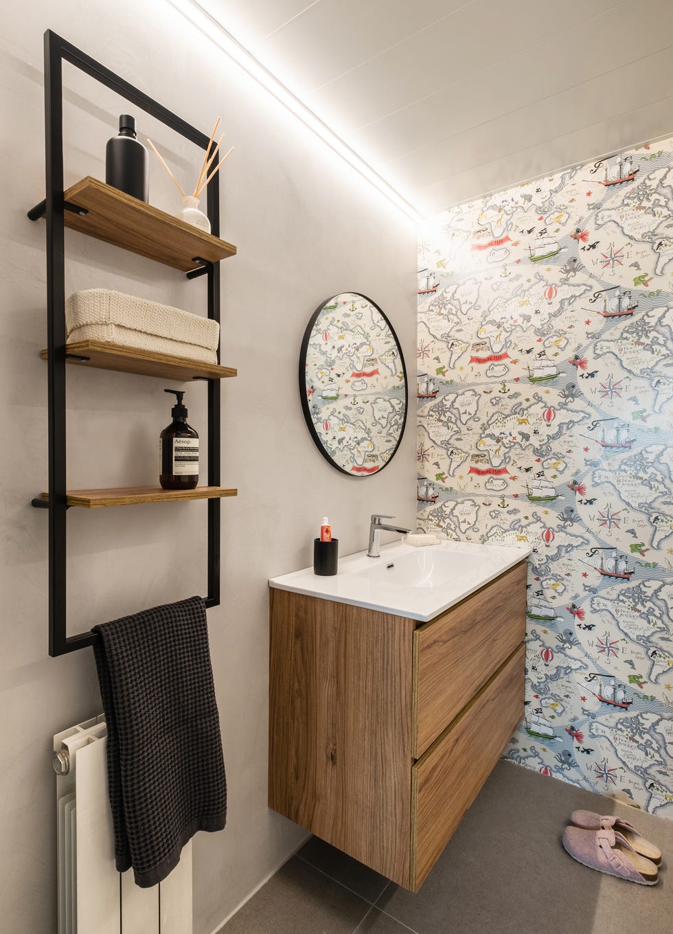 baño infantil con mueble de madera suspendido, estantería de pared industrial y papel pintado con un mapamundi