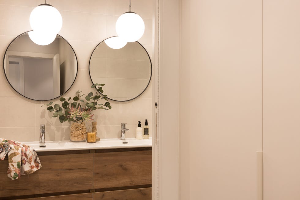 baño con mueble suspendido de madera y dos espejos redondos con marco metálico