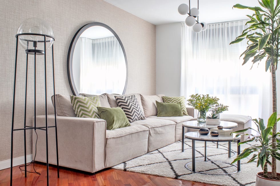 salón moderno con sofá beige, mesas nido con sobres de mármol, espejo redondo y lámpara de pie de metal negro