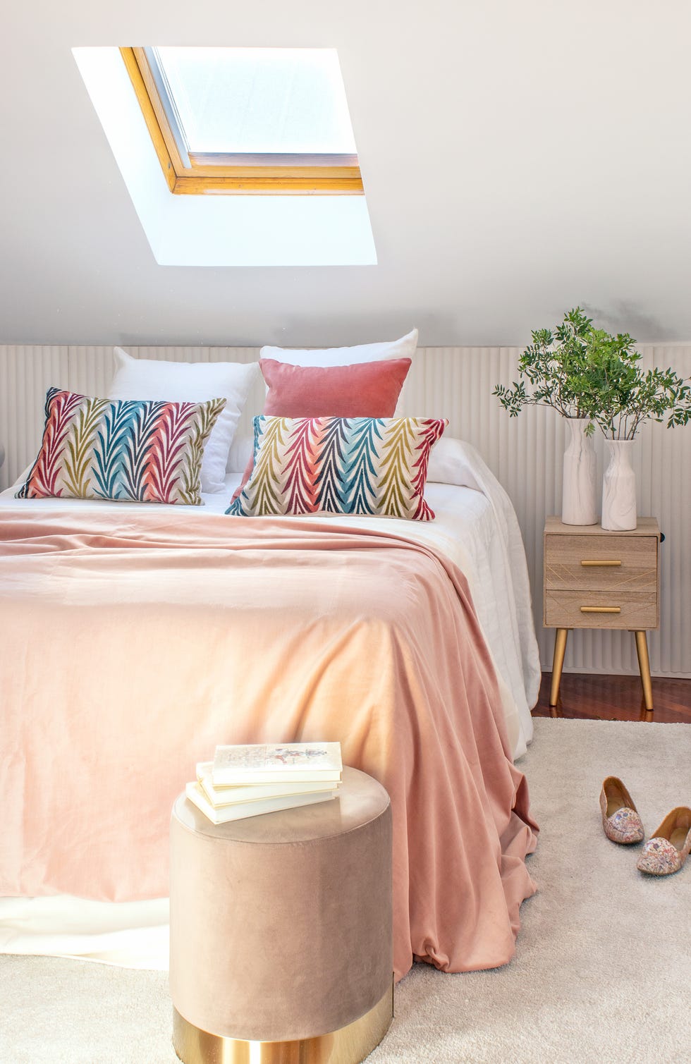 dormitorio femenino abuhardillado con panel a medida, puf de terciopelo rosa, alfombra de pelo blanco y mesita de noche de diseño mid century