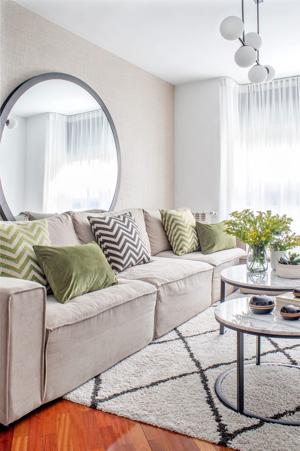 salón moderno con sofá beige, mesas nido con sobres de mármol, espejo redondo y lámpara de bolas