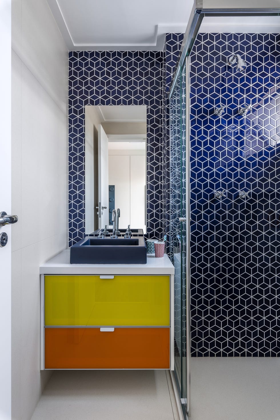 baño moderno con azulejos geométricos de color azul en la pared de la ducha y mueble bajo lavabo con cajones de colores
