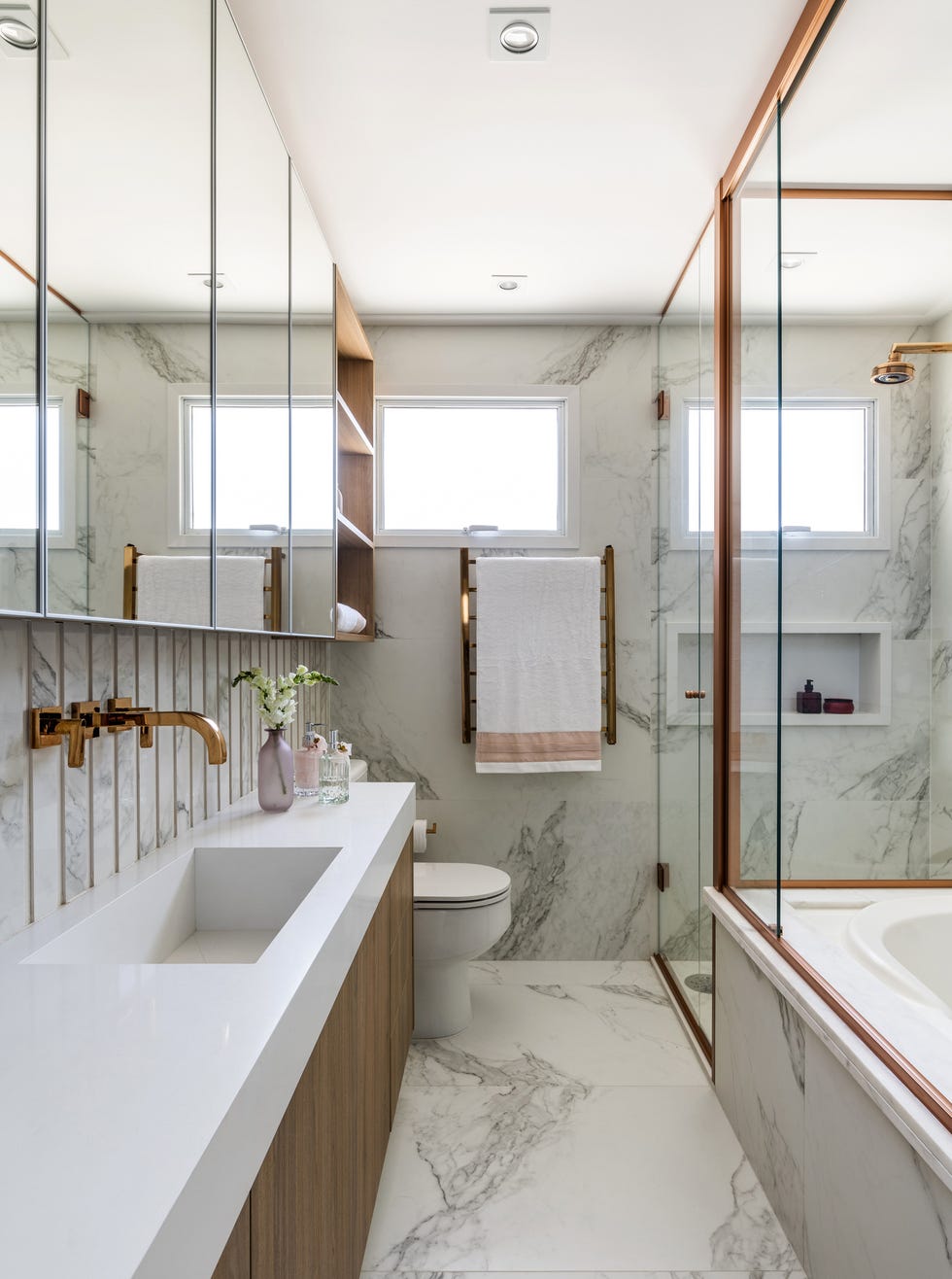 baño con bañera y revestimientos de mármol con detalles de metal dorado