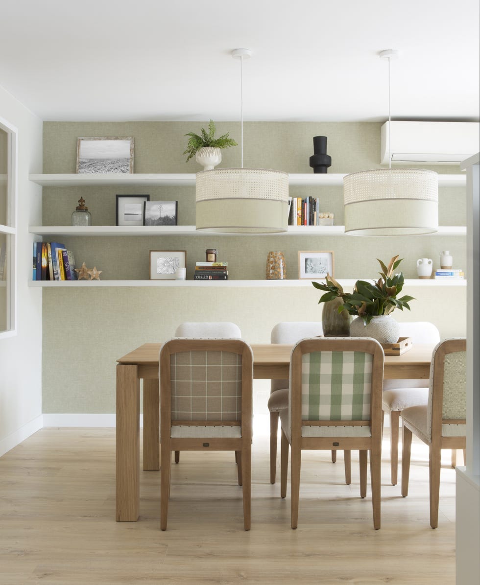 comedor con mesa de madera, sillas tapizadas con tela a cuadros, lámparas suspendidas de rejilla blanca y baldas en las paredes