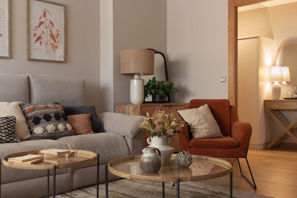 salón con sofá rinconera beige, mesas de centro redondas y butaca de terciopelo terracota