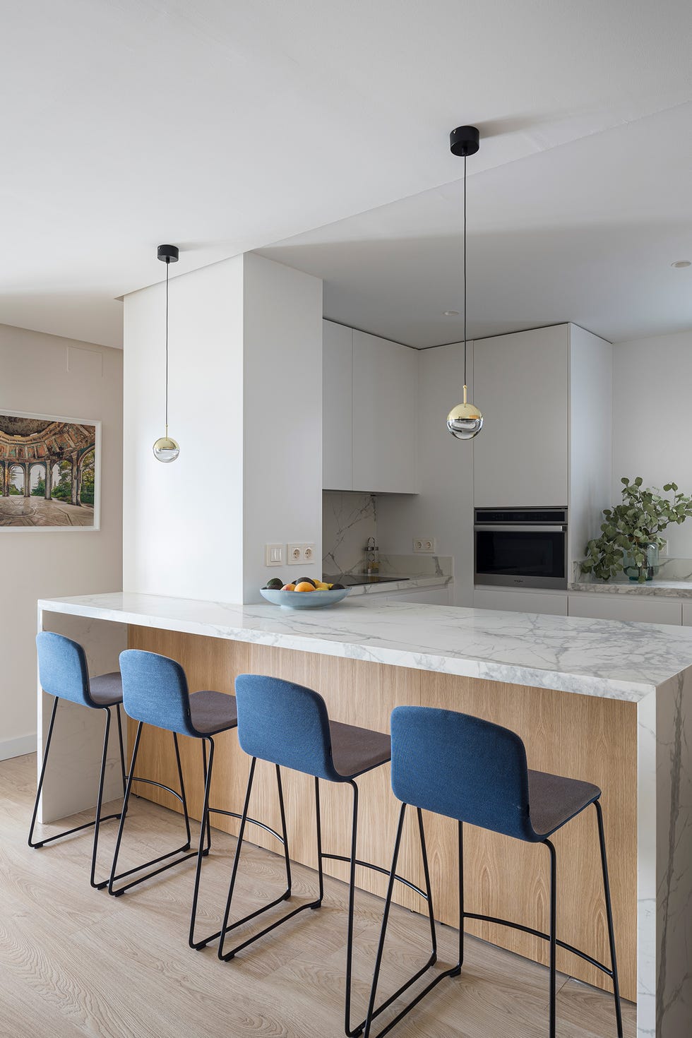 cocina abierta con península de mármol y madera y taburetes azules
