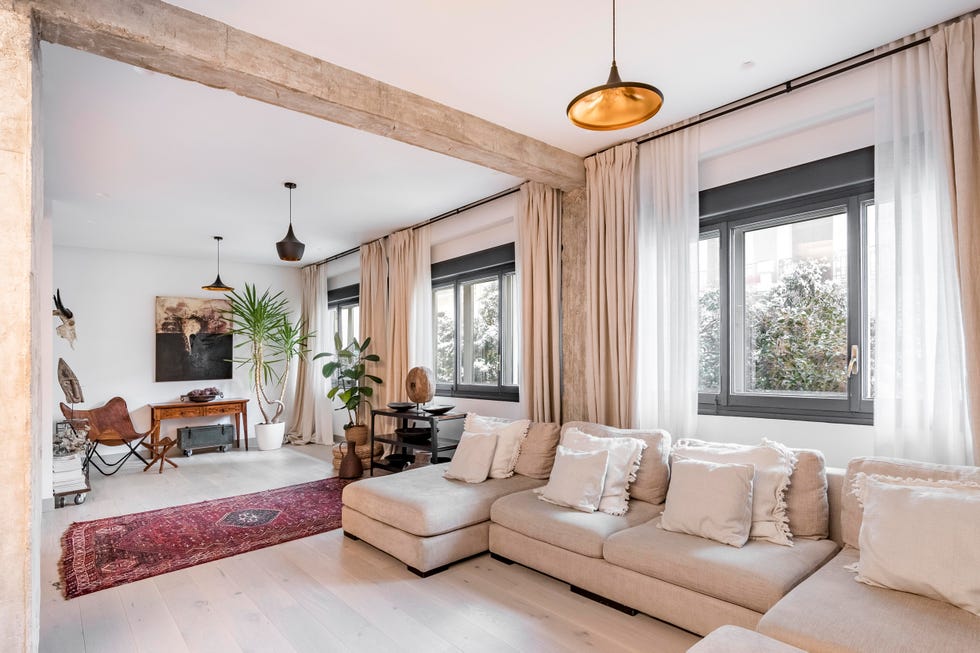 salón abierto con vigas y columnas vistas de cemento decorado en tonos neutros con un sofá modular beige