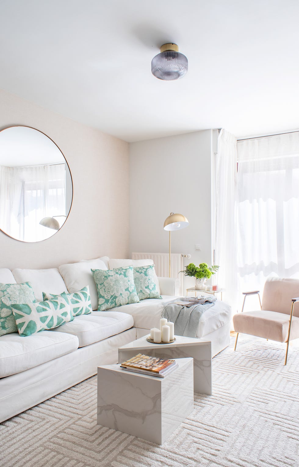 salón con sofá blanco con chaise longue, mesas de centro de mármol y butaca de terciopelo rosa