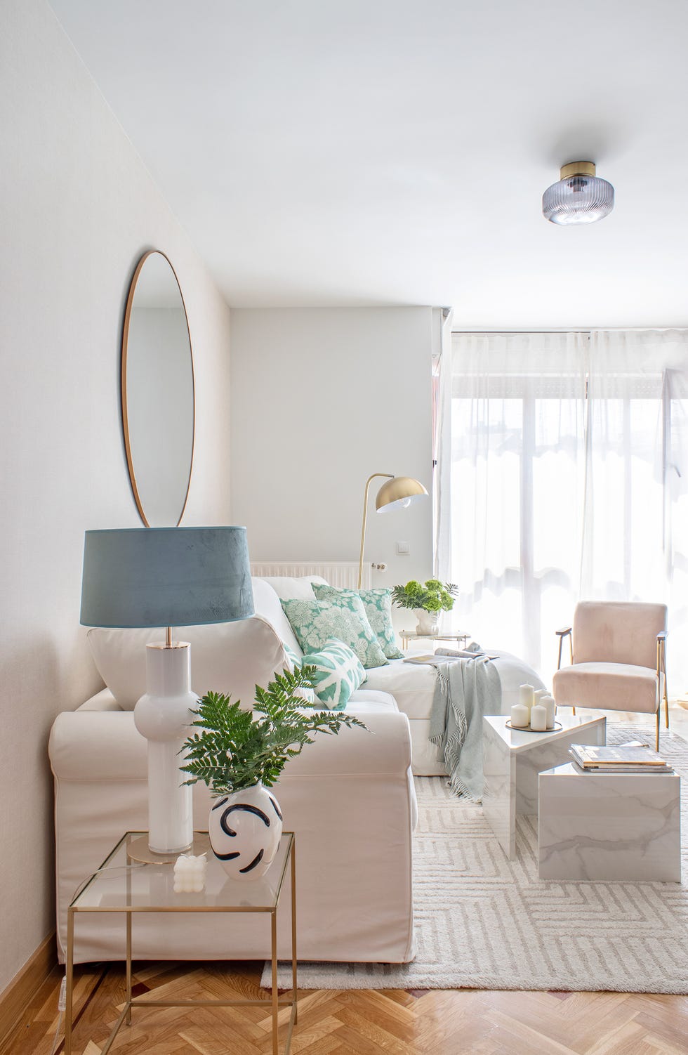 salón con sofá blanco con chaise longue, mesas de centro de mármol y butaca de terciopelo rosa