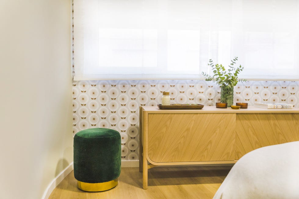 dormitorio decorado con papel pintado setentero y un puf tapizado en terciopelo