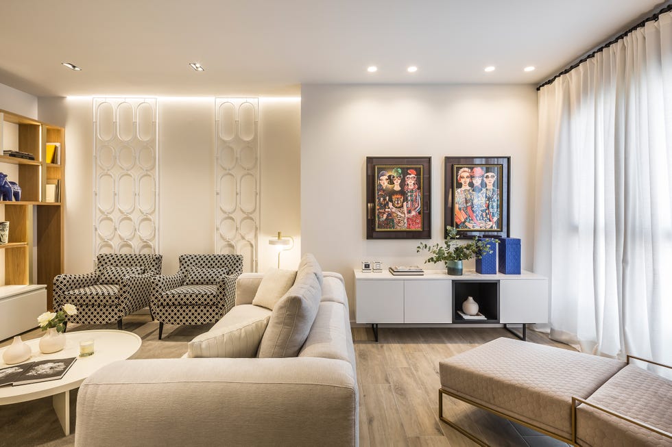 salón de diseño moderno con sofá beige, butacas con motivos geométricos, mesa de centro blanca y aparador blanco con dos cuadros en la pared