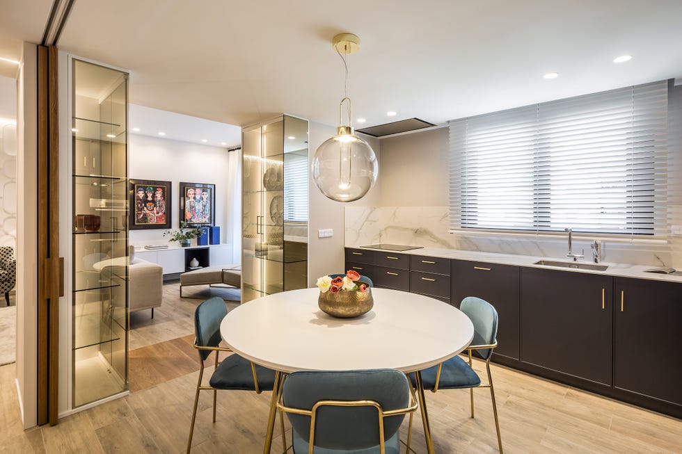 mesa de comedor redonda con sillas de terciopelo azul y patas doradas dentro de la cocina con frentes de armarios grises