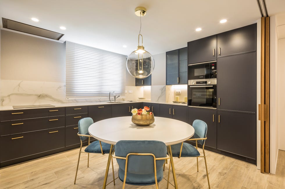 mesa de comedor redonda con sillas de terciopelo azul y patas doradas dentro de la cocina con frentes de armarios grises