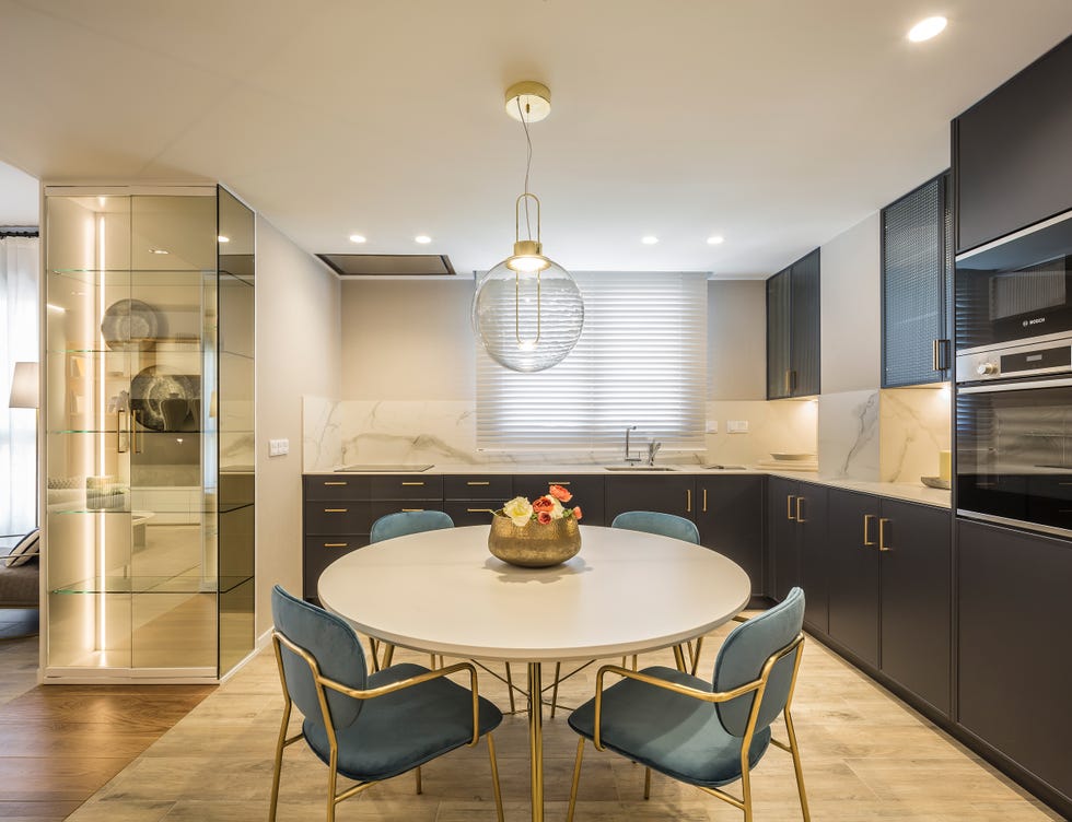 mesa de comedor redonda con sillas de terciopelo azul y patas doradas dentro de la cocina con frentes de armarios grises