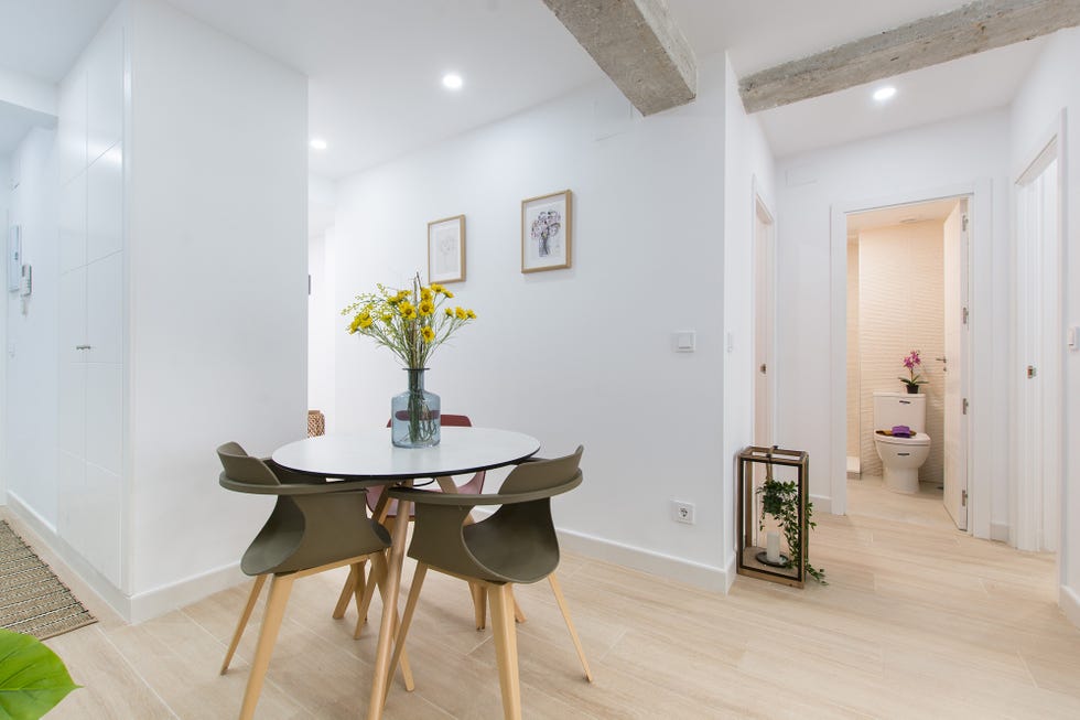 comedor abierto de diseño nórdico con una mesa blanca redonda y tres sillas de colores