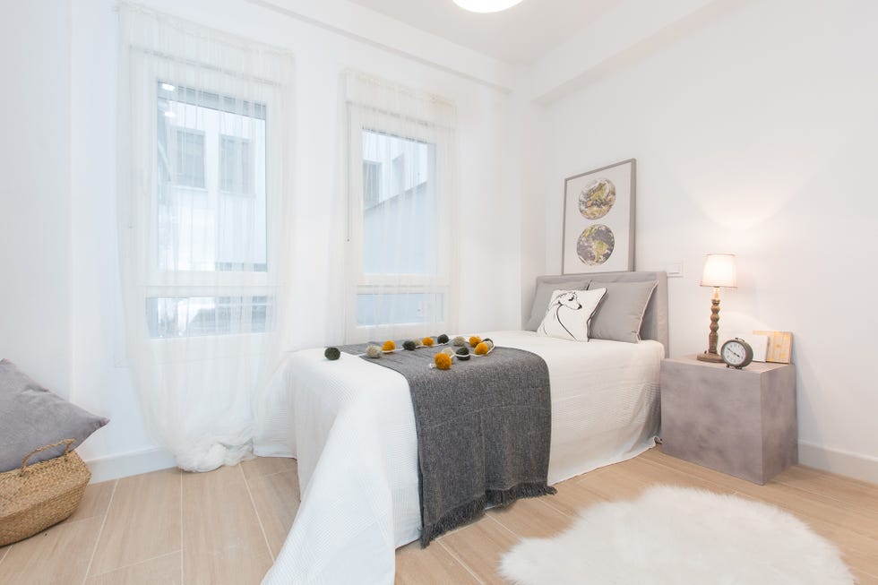 dormitorio con cama individual, cabecero gris a juego con los cojines y la mesilla de noche, y alfombra de pelo blanco