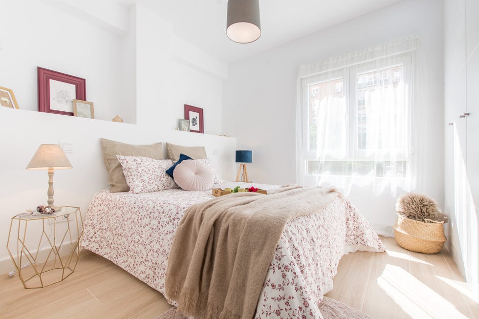 dormitorio con cama de matrimonio, colcha de flores, y cabecero de obra dividido en dos por un tabique