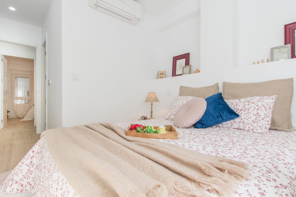 cama de matrimonio con colcha de flores y cabecero de obra dividido en dos por un tabique