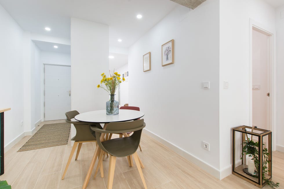 comedor abierto de diseño nórdico con una mesa blanca redonda y tres sillas de colores