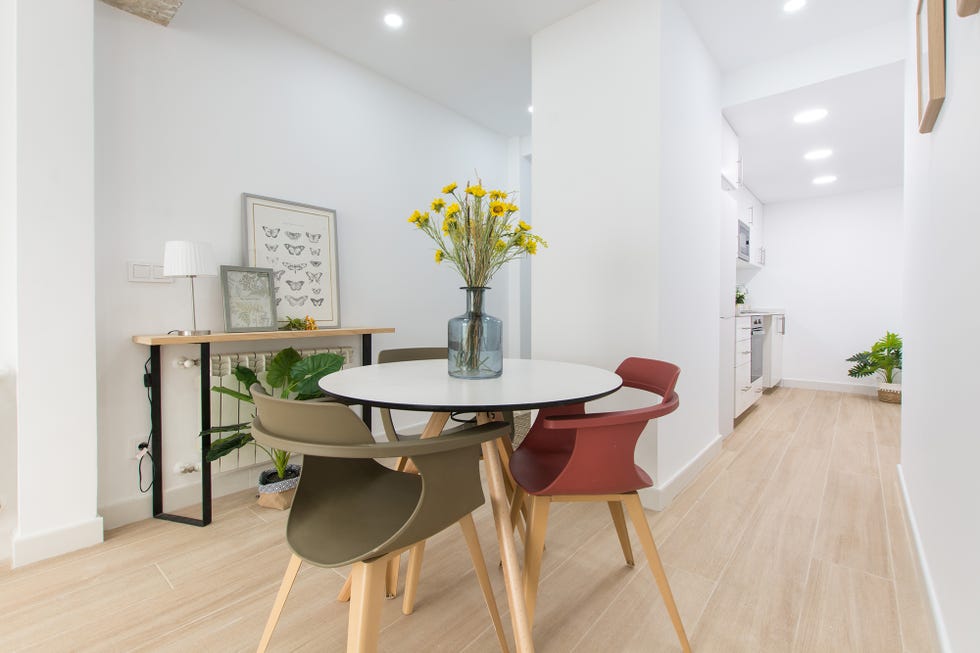 comedor abierto de diseño nórdico con una mesa blanca redonda y tres sillas de colores