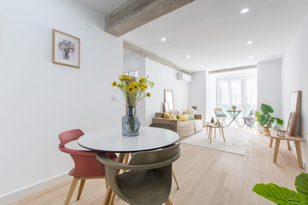 comedor abierto de diseño nórdico con una mesa blanca redonda y tres sillas de colores