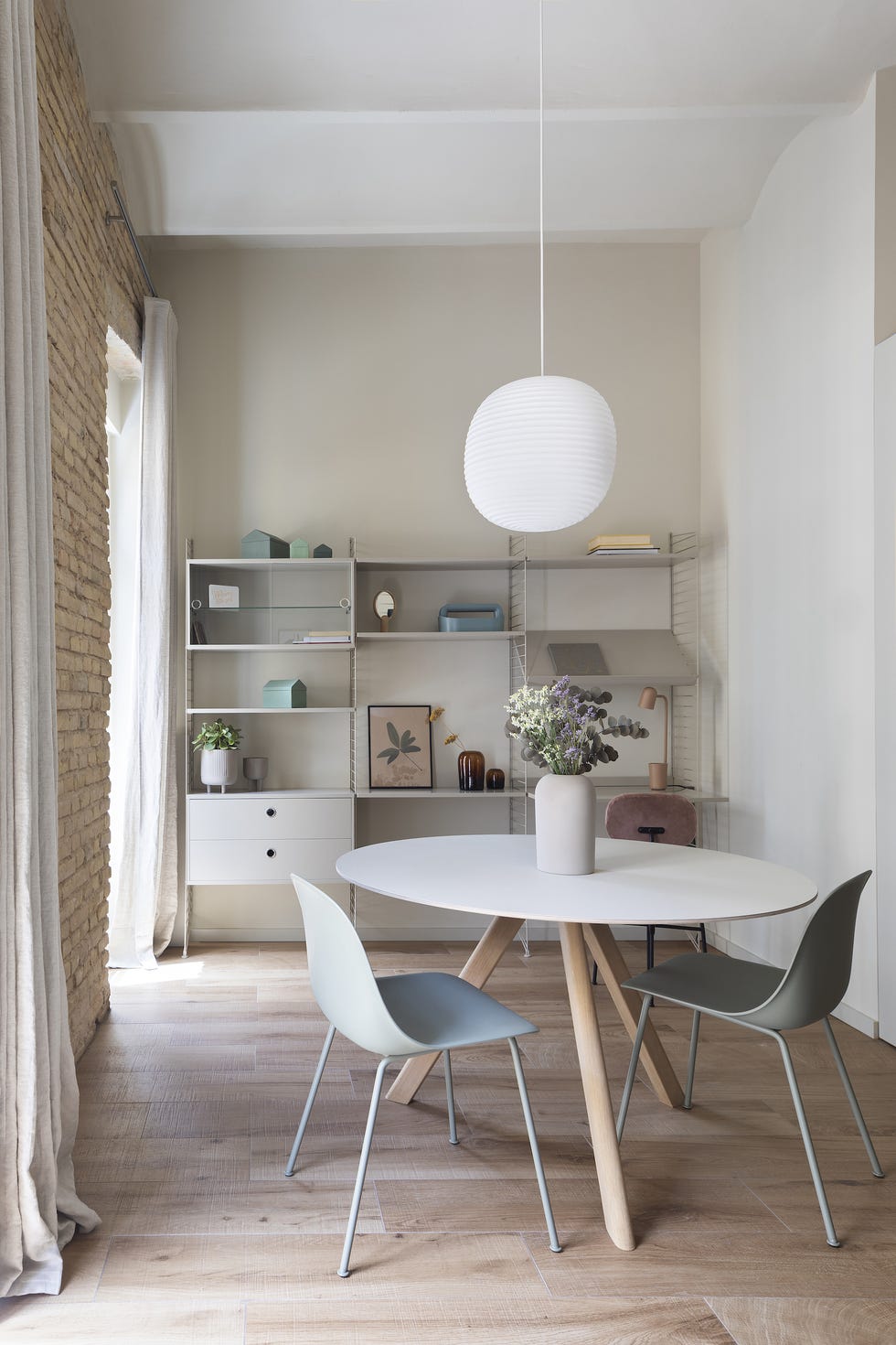 mesa de comedor redonda con sobre blanco, sillas de color empolvado y estantería nórdica