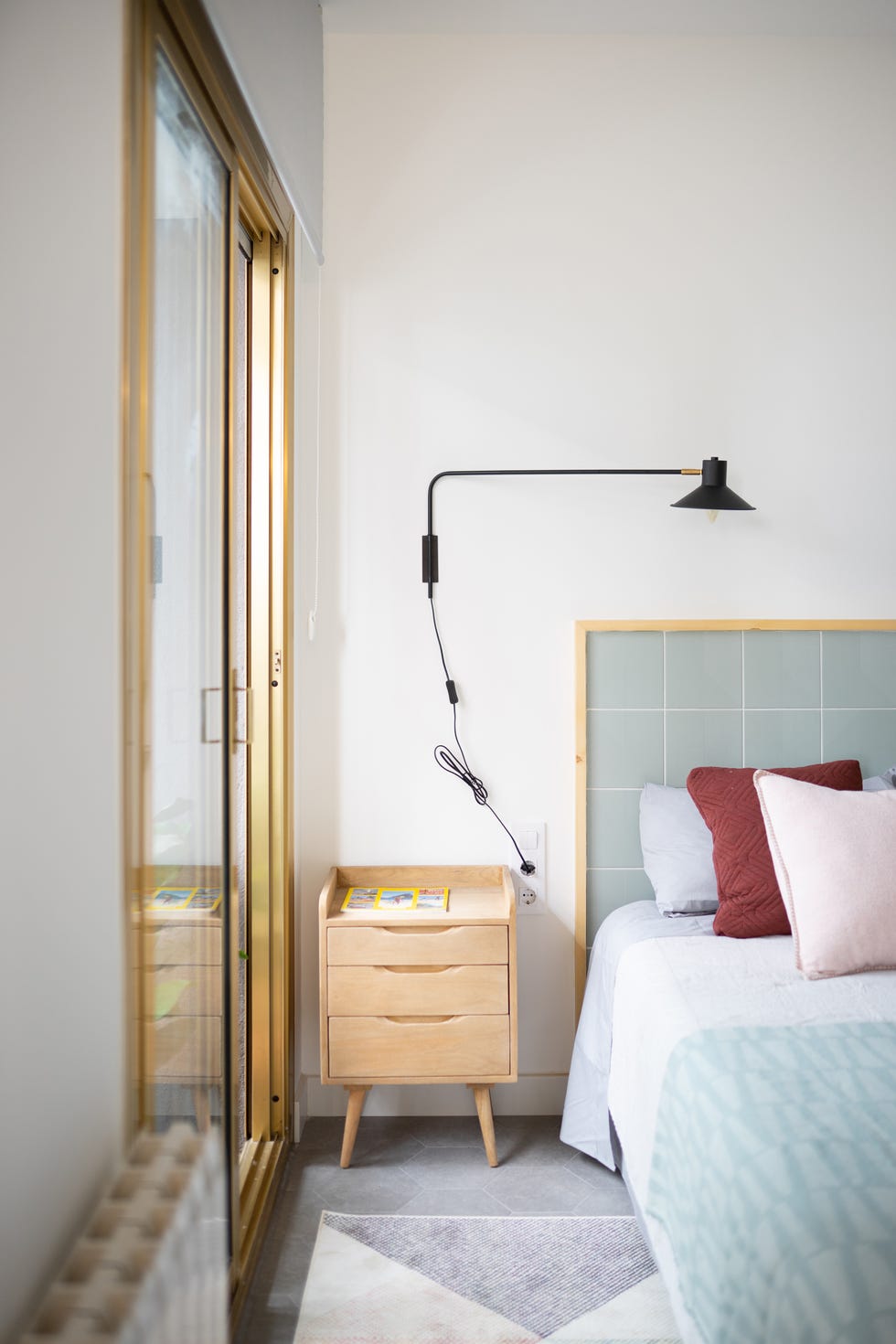cama con cabecero de azulejos y marco de madera, mesita nórdica de madera y aplique metálico negro