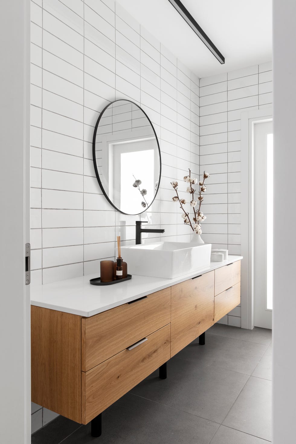 baño moderno con mueble de lavabo de madera, azulejos blancos tipo metro, grifo negro mate y espejo con marco redondo