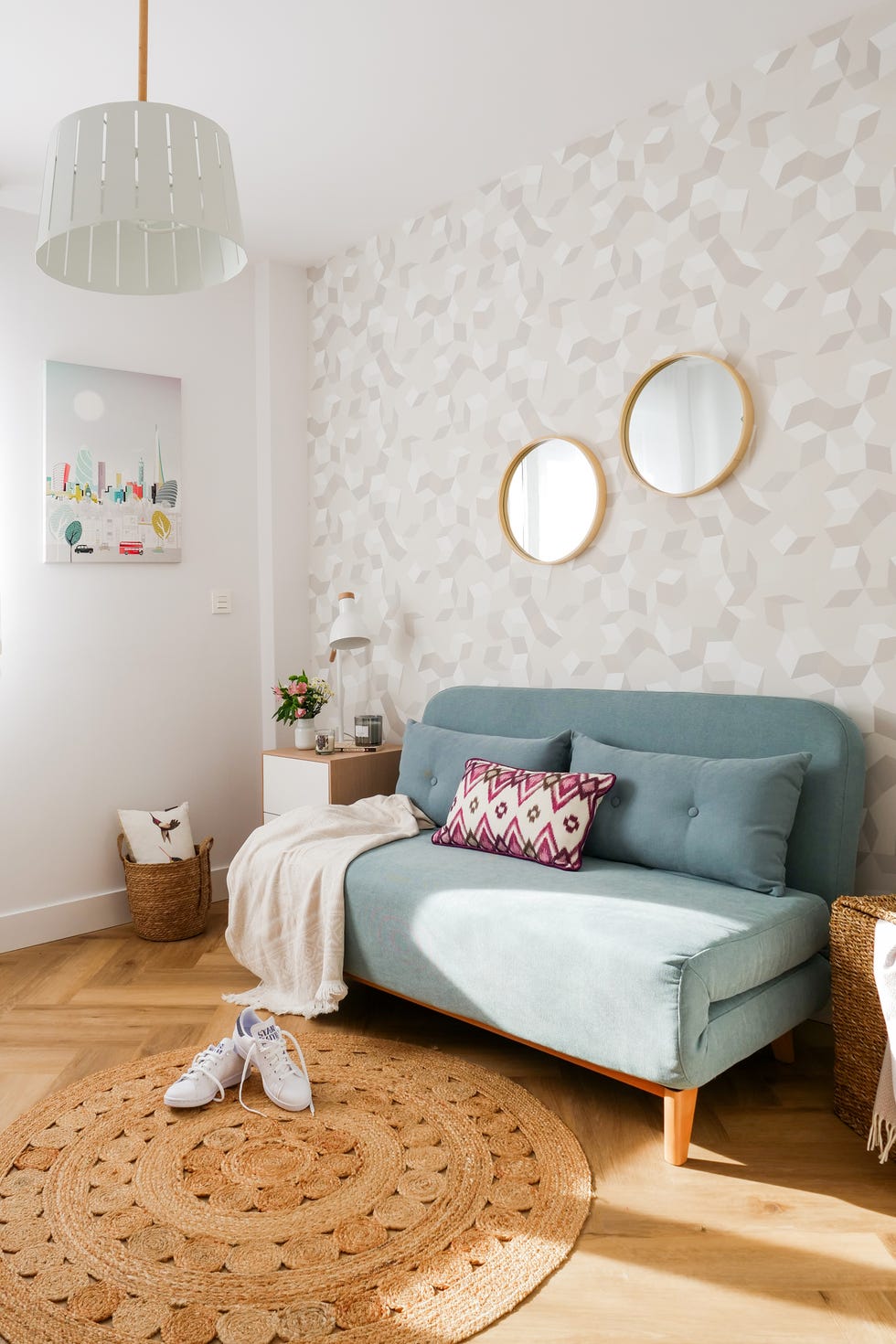 habitación con sofá cama verde, alfombra redonda de yute y papel pintado con motivos geométricos en gris