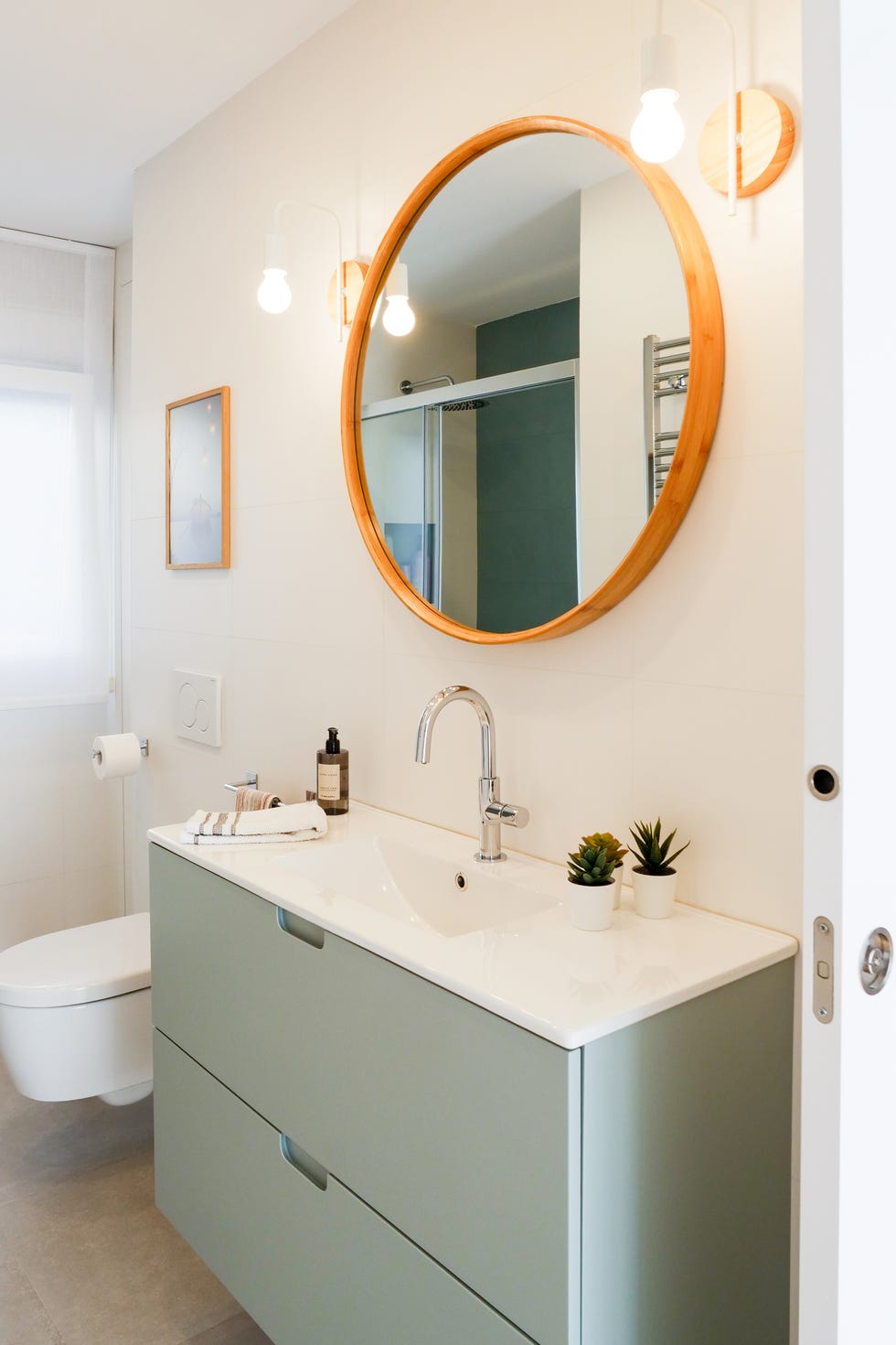 baño con mueble bajolavabo en color verde suspendido y espejo co marco redondo de madera