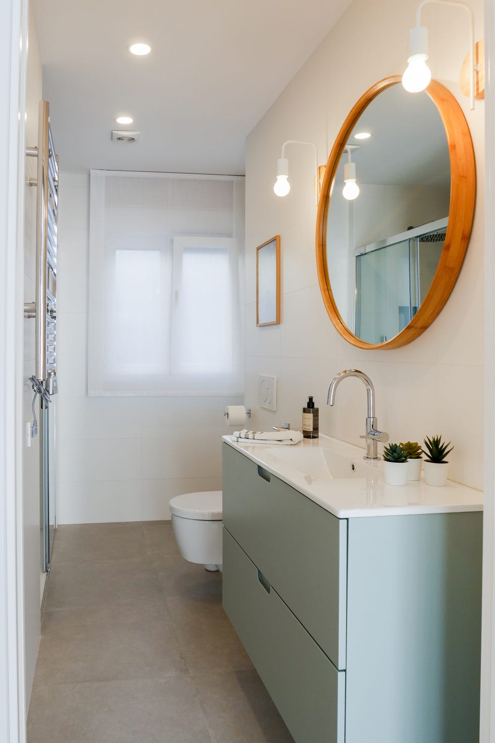 baño con mueble bajolavabo en color verde suspendido y espejo co marco redondo de madera