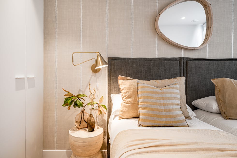 dormitorio decorado en beige y gris con cabecero de tela y taburete de madera como mesilla de noche