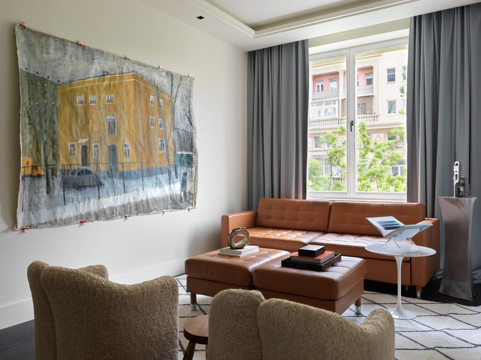 salón moderno con sofá de piel capitoné a juego con los reposapiés y tapiz sobre la pared