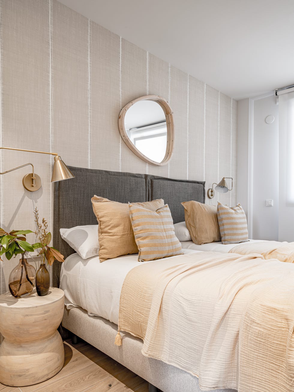 dormitorio decorado en beige y gris con cabecero de tela y taburete de madera como mesilla de noche
