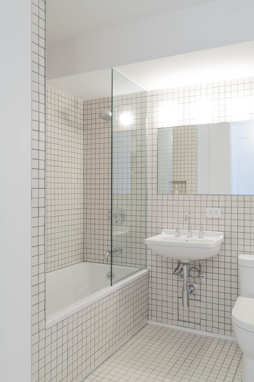 baño con bañera revestido con azulejos de cuadrícula blancos
