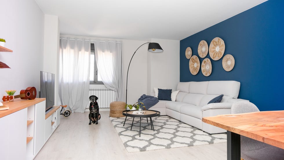 salón con sofá con chaise longue gris, mesas nido, puf de yute y pared azul