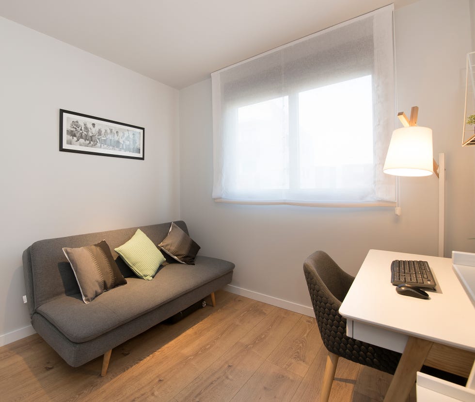 despacho de estilo nórdico con sofá cama gris y mesa de escritorio en color blanco