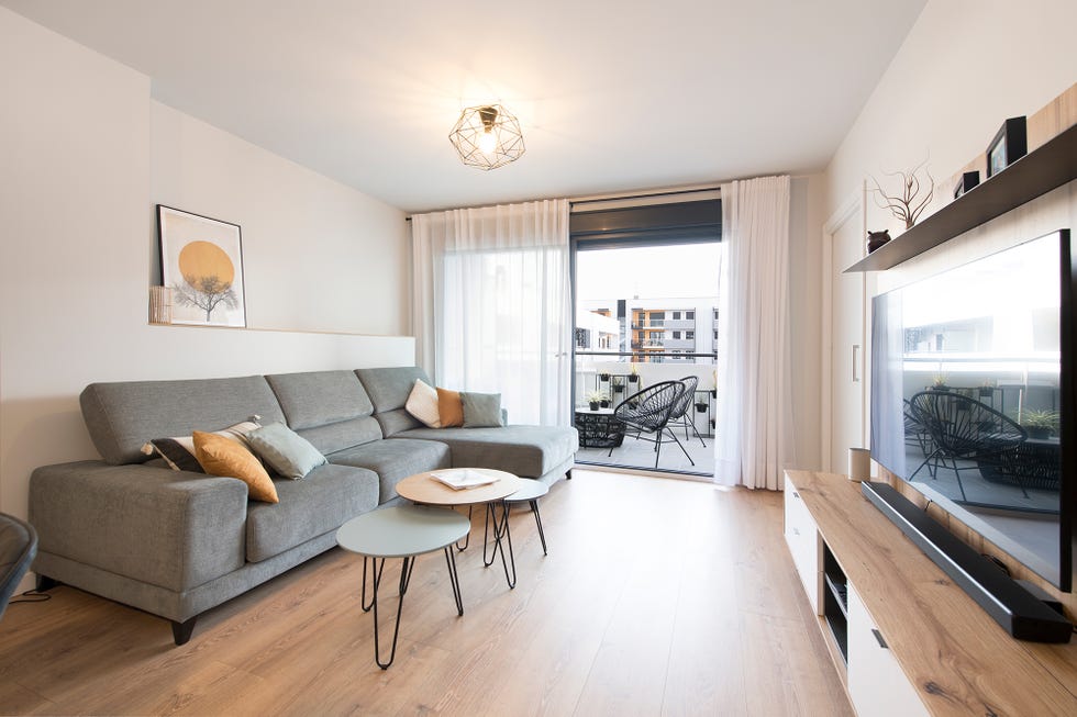 salón con sofá con chaise longue tapizado en gris, mesas encastrables y acceso a la terraza
