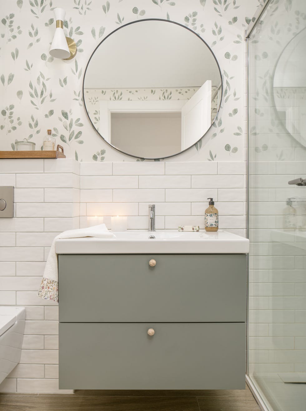 mueble de baño verde, azulejos blancos tipo metro y papel pintado con motivos botánicos