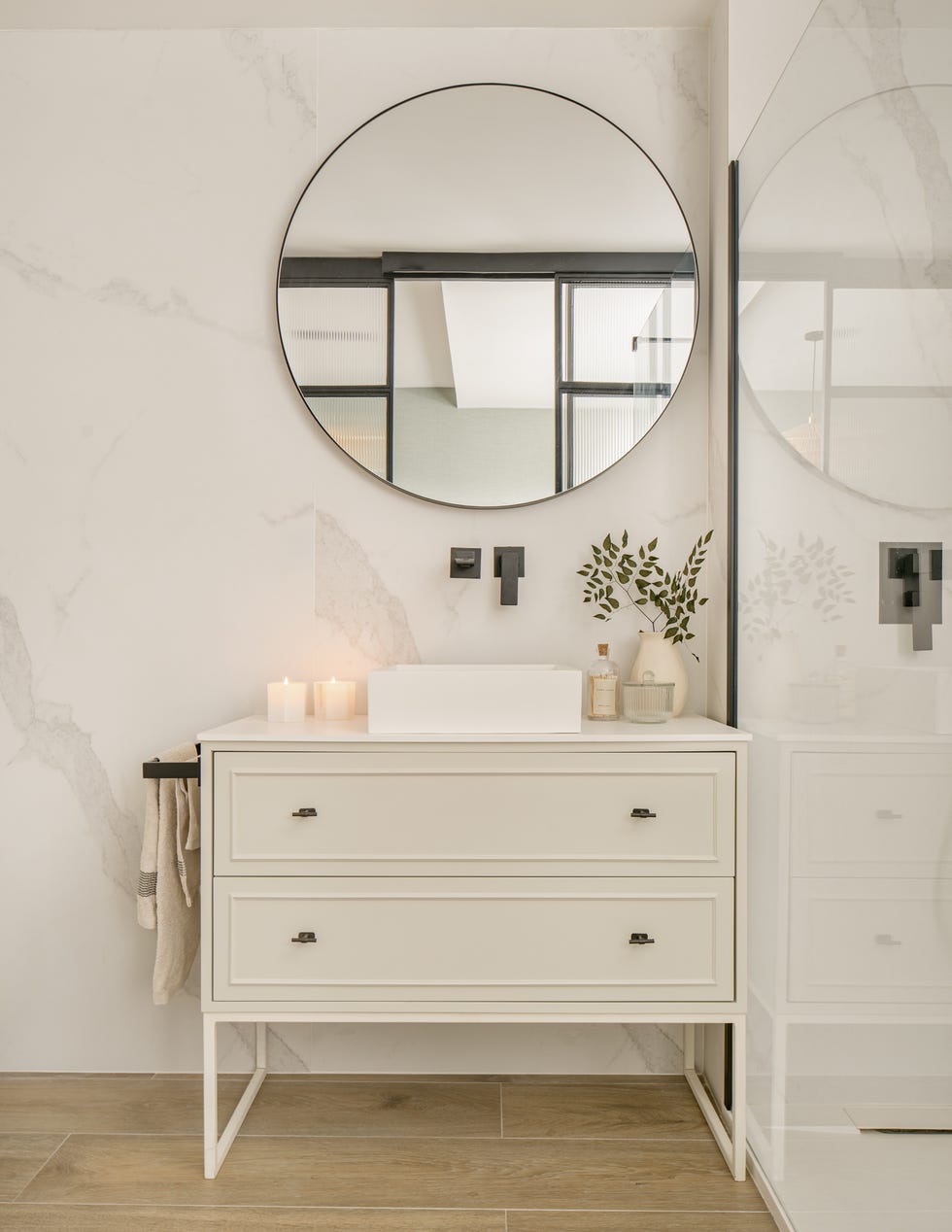 mueble de baño blanco, espejo redondo y revestimiento de mármol