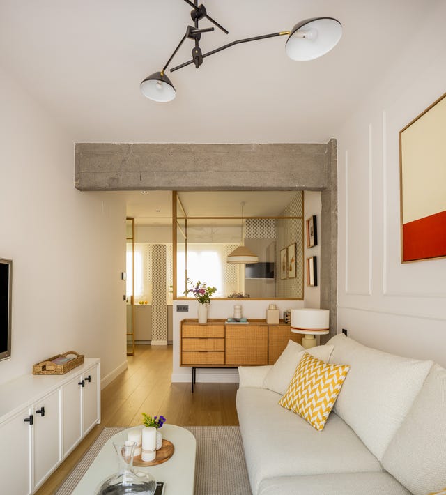 salón con sofá tapizado en beige, aparador de madera y cerramiento de cristal